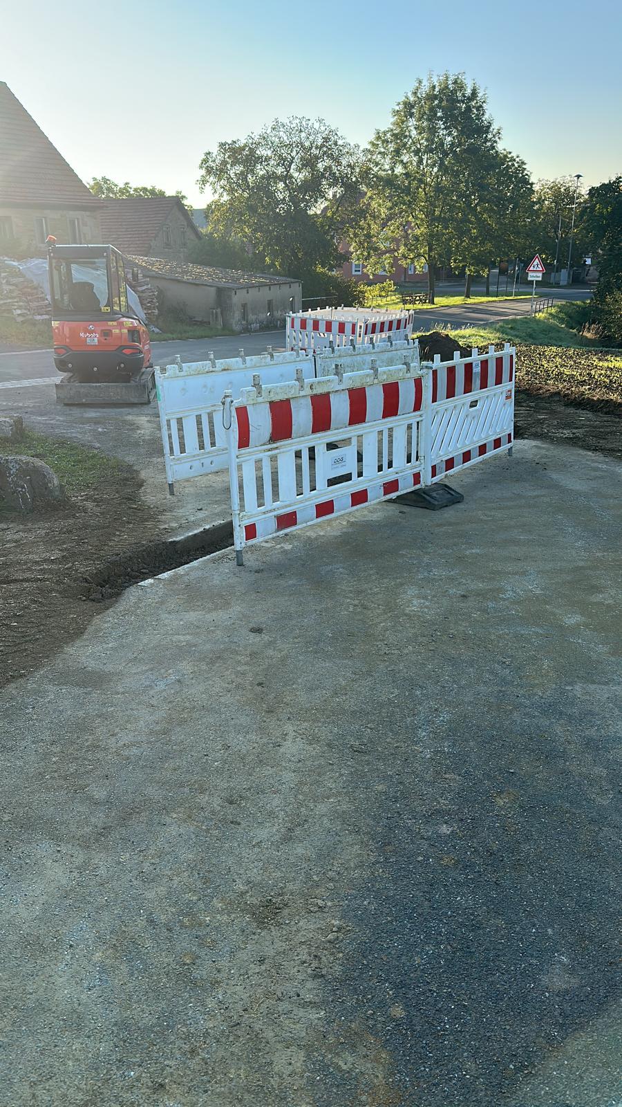 MTHH GbR - Kabeltragsystembau, Regalbau/Prüfung und Tiefbau - Eine Baustelle in ländlicher Gegend mit rot-weißen Sicherheitsbarrieren, die einen offenen Graben auf einem unbefestigten Weg umgeben.