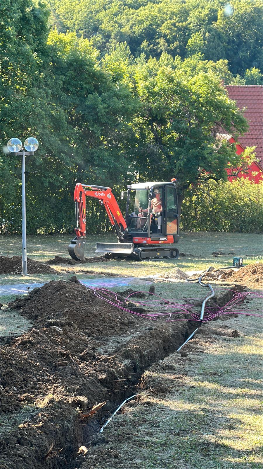 MTHH GbR - Kabeltragsystembau, Regalbau/Prüfung und Tiefbau - Ein Kubota-Minibagger hebt in einer Grasfläche einen schmalen Graben zum Verlegen von Kabeln oder Rohren aus.
